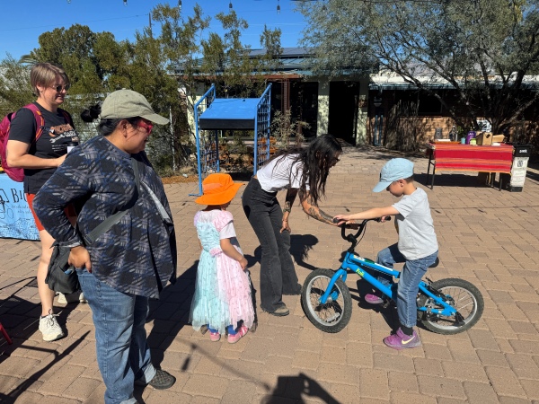a group of adults and kids enjoying a sustainable mobility event, with one kid riding a blue bike