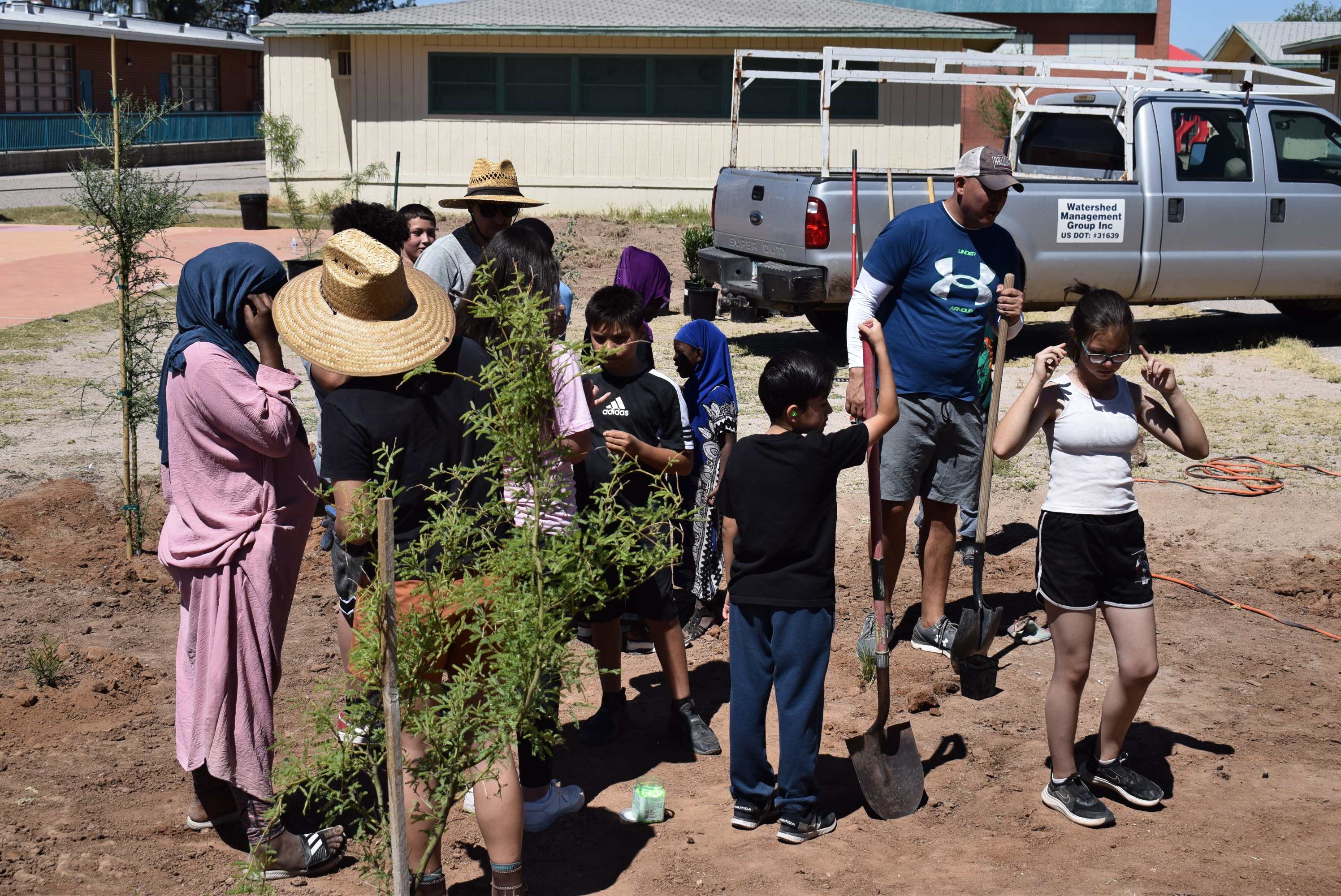 A group of students and volunteers around small newly planted trees
