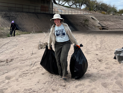 A young woman in a bucket hat pulls two bags of trash out of the river bed