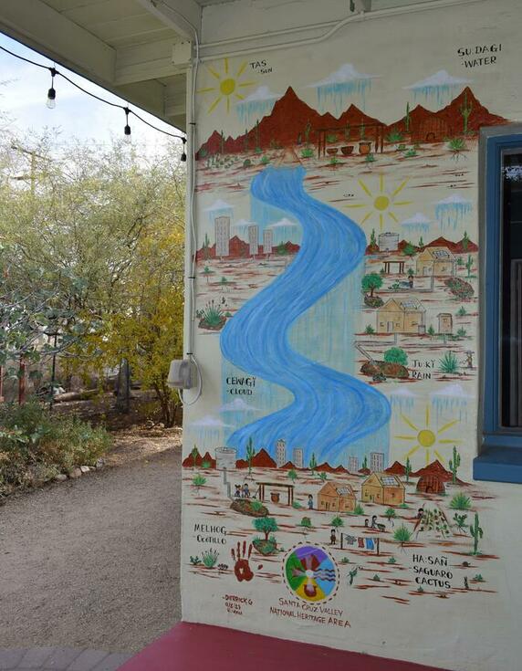 A mural with a river running through it vertically, mountains at the top and people and plants along the sides