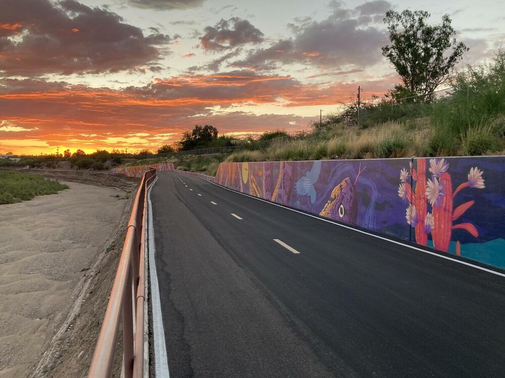 A bike path with colorful murals on the wall and the sunset in the distance