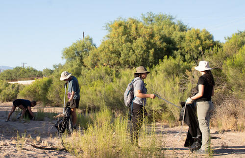 A group of people with reacher-grabbers pick up trash in a dry riverbed