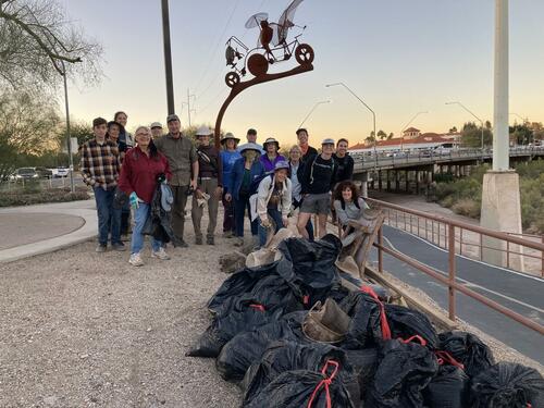 A group of volunteers stand behind a dozen bags of trash