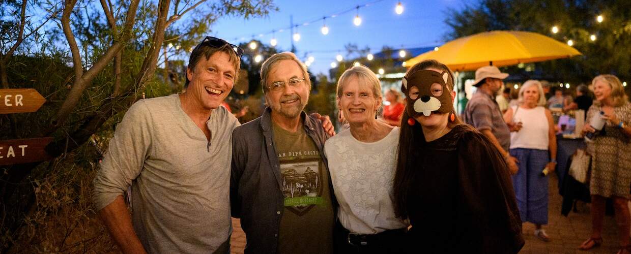 Four people smile at the camera in the evening -- one is wearing a beaver mask