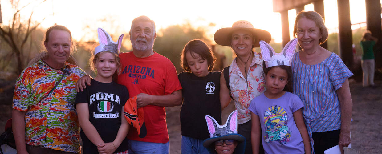 A group of mixed age people smile in front of sunset 