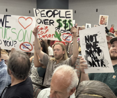 A crowd of people hold signs advocating against a data center