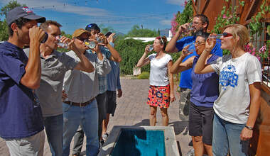 A group of people stand around the open top of an underground cistern--they are all drinking glasses of rainwater