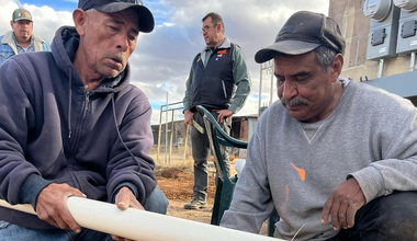 Two men in sweatshirts and ball caps heat a pvc pipe